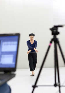 A computer and camera tripod in the forground capturing a female dancer in the background