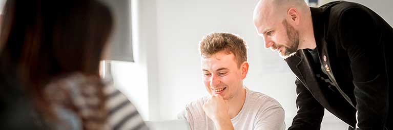 Smiling man looking down, with another man leaning over to look at same thing