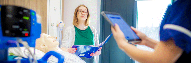 Two nurses examine a patient dummy on a ward.