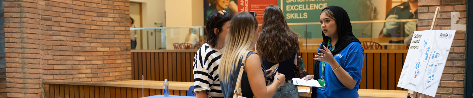 Mother and a future student are attending a Coventry University open day and are at the information point talking to a nursing student wearing a nurse uniform.