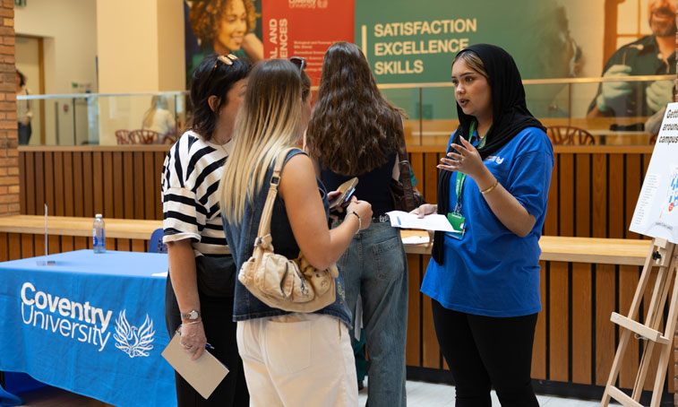 Mother and a future student are attending a Coventry University open day and are at the information point talking to a nursing student wearing a nurse uniform.