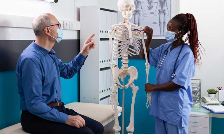 a nurse using a model skeleton to explain a diagnosis to a patient