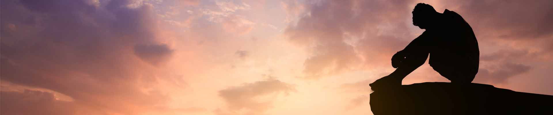 Silhouetted photo. Lonely man sitting on cliff watching the evening glow.