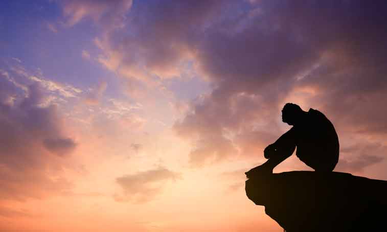Silhouetted photo. Lonely man sitting on cliff watching the evening glow.