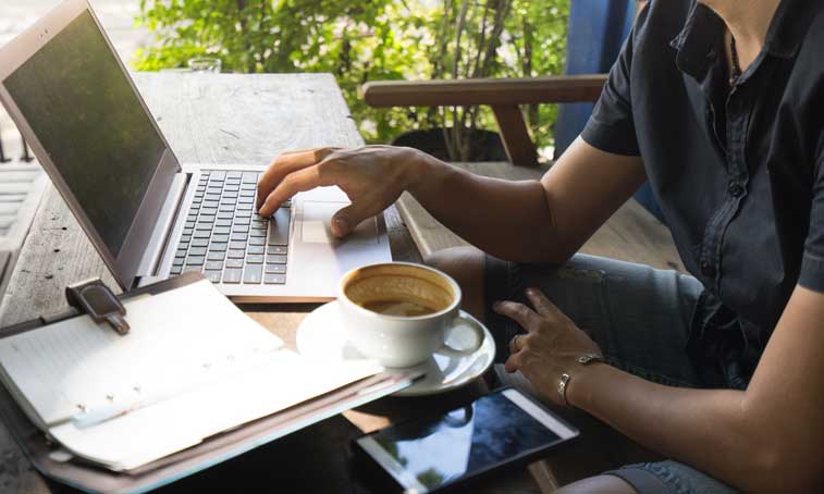 creative freelancer working from the remote location on a laptop with a notebook and a cup of coffee on the side