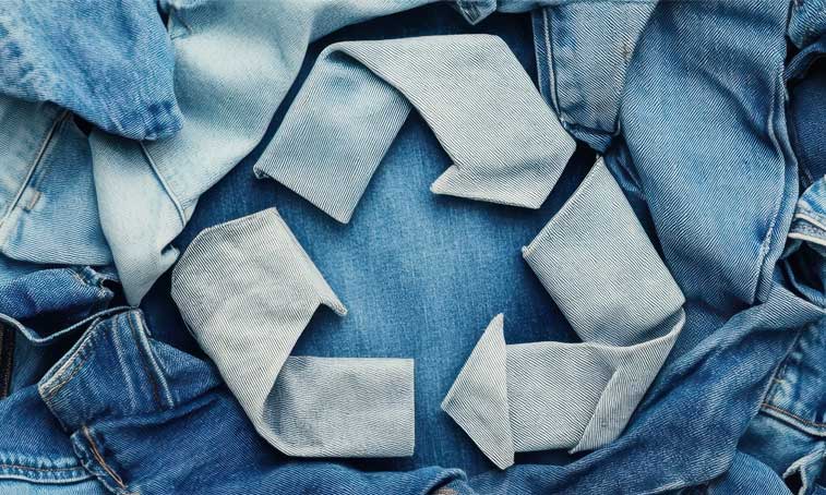 recycle symbol made of denim material on top of pile of discarded jeans