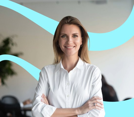Smiling woman in a white shirt standing with arms crossed in an office.