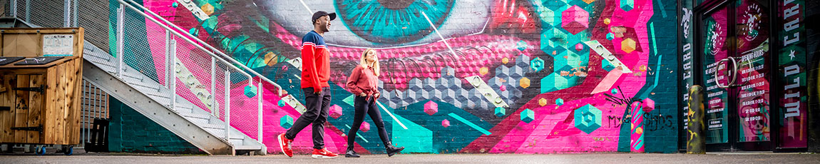 Two students walking past bright, modern street art in Coventry's Fargo Village.