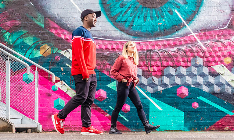 Two students talking whilst walking past street art