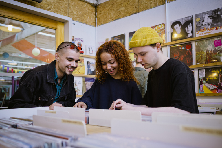 3 students scrolling through reccords in shop