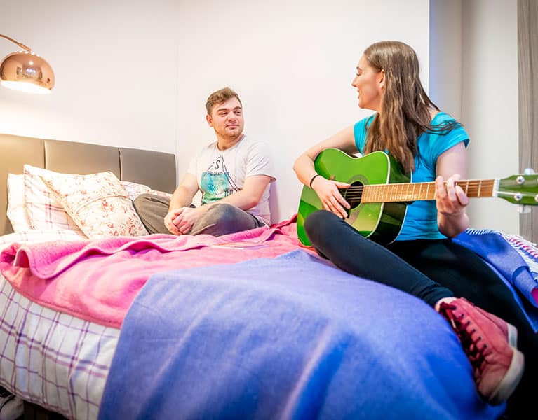 Student sitting in accommodation playing a guitar