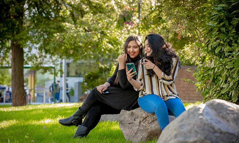 2 female students sat outside looking at a mobile phone