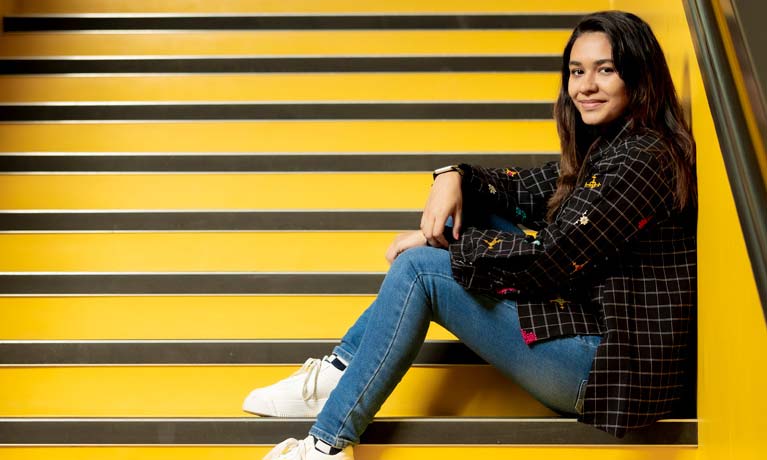 female student smiling at a camera sitting on a stairwell