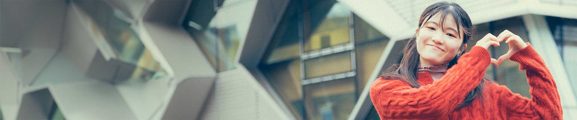 female student standing in front of the EEC building making a heart shape with her hands
