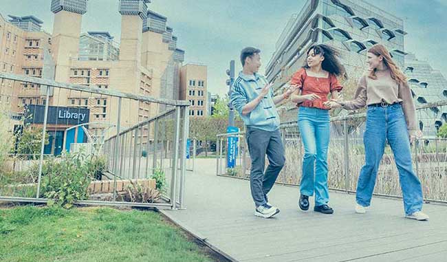 Three students walking on campus with library building in the background 