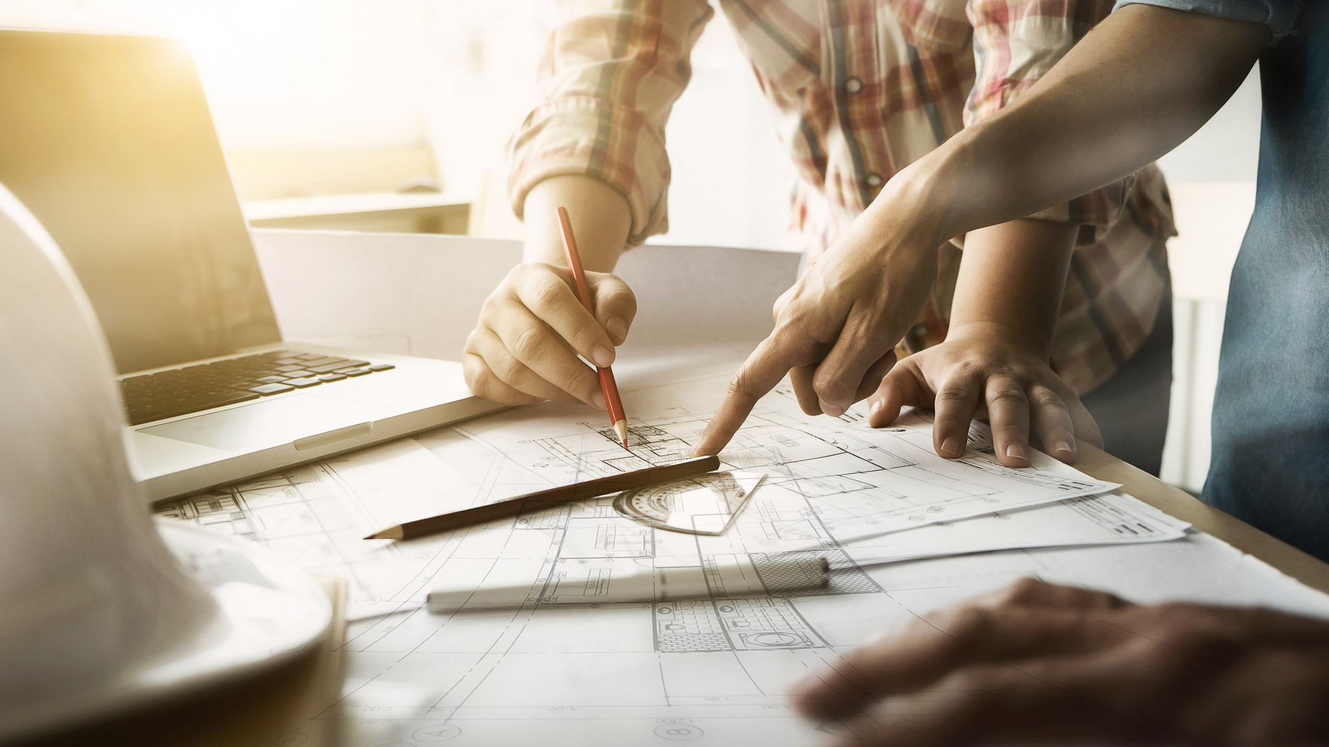 Table filled with technical drawings and hands pointing at elements on the papers