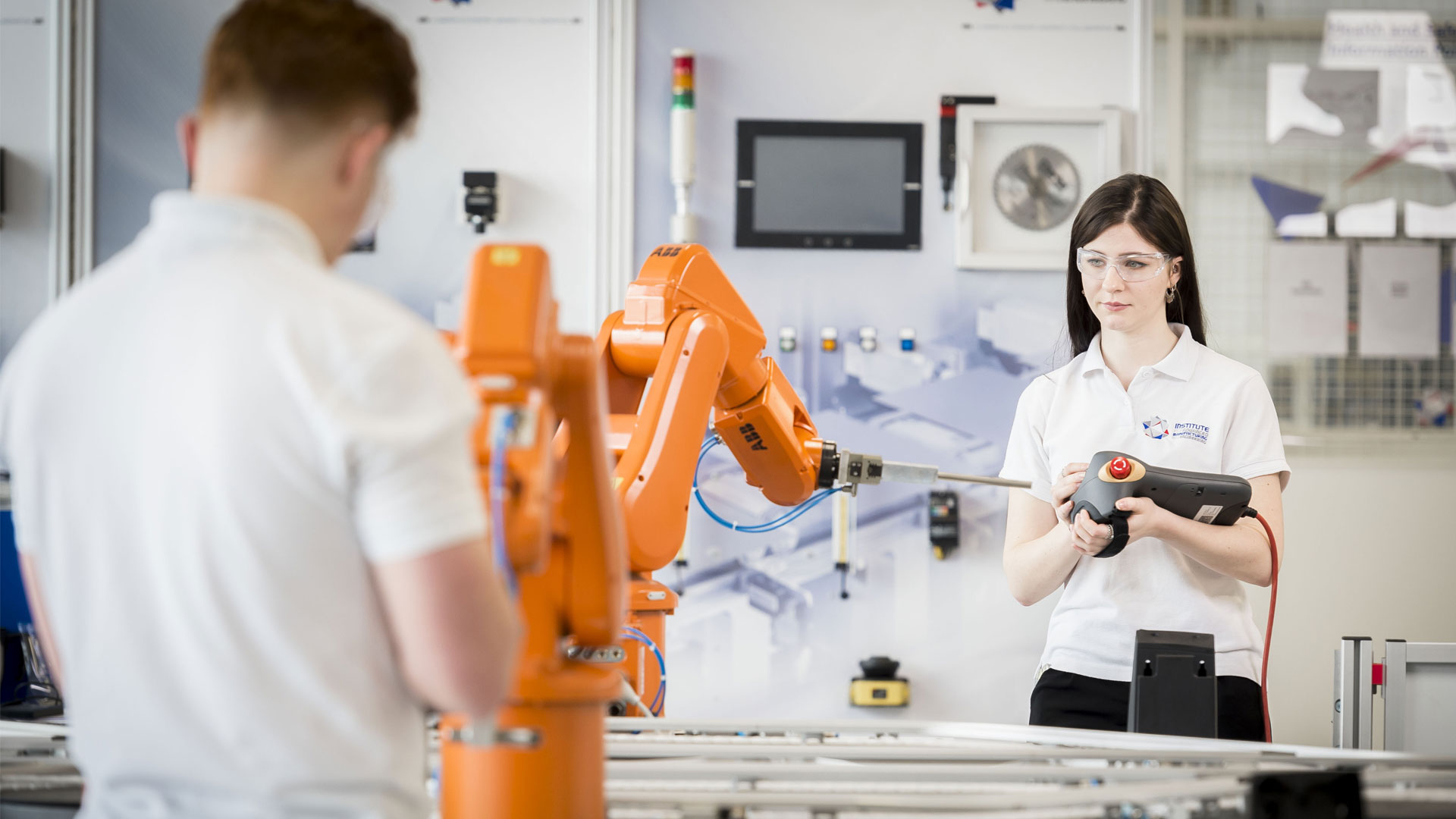 A student in a Manufacturing Engineering lab using the controller for the equipment and wearing safety glasses