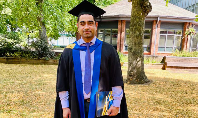 A student in his graduation cloak and hat stood outside.