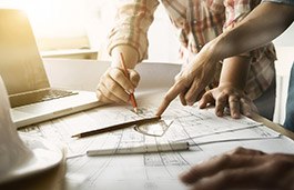 Table filled with technical drawings and hands pointing at elements on the papers