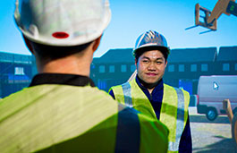 Two people at work talking to each other wearing fluorescent jackets and helmets