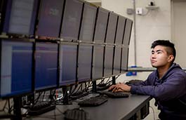 male student looking at a double bank of computer monitors