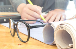 Close up of hands working on paperwork on a table with glasses and rolls of paper in the foreground