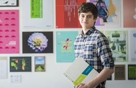 Student holding their portfolio in front of a wall of students' graphic design works 