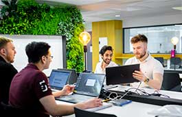 Four students sat at a table with laptops talking