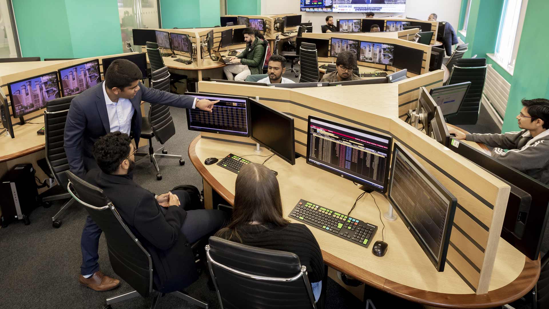 A lecturer assisting two students on the Trading Floor