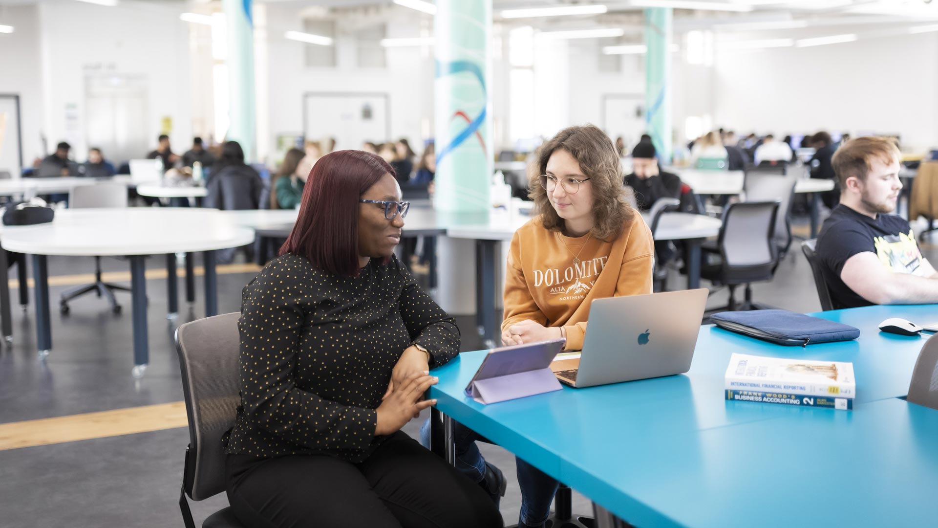 Students working on a laptop in an open plan study area