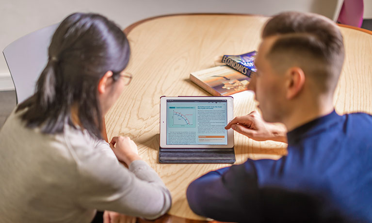 Two lecturers sitting at a table discussing what they can see on the tablet.