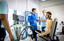 Student on an exercise bike with other students observing and taking notes