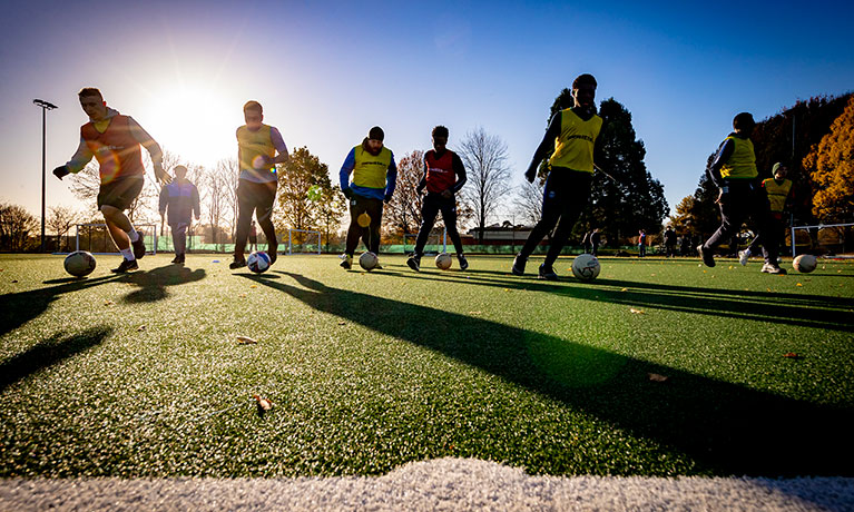 Students in football gear and bibs running on a pitch