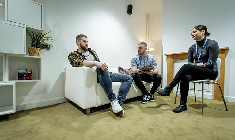 Three students sat talking in community house living room.