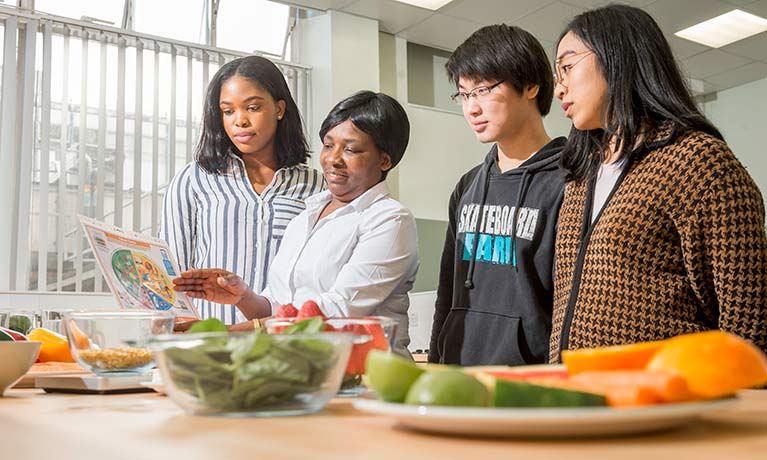 lecturer showing students a food chart in front of plates of fruit and vegetables