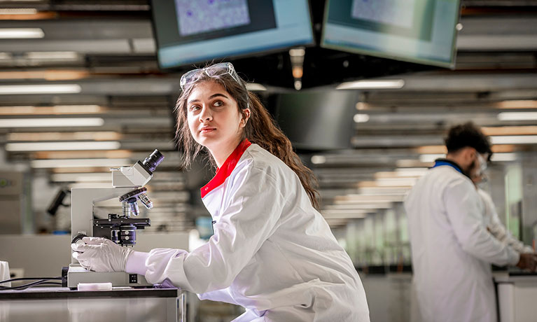 Young female wearing a white coat looking through a microscope