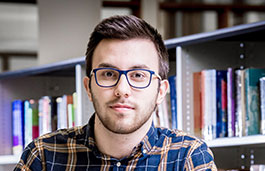 Male student sat in front of a shelf of books