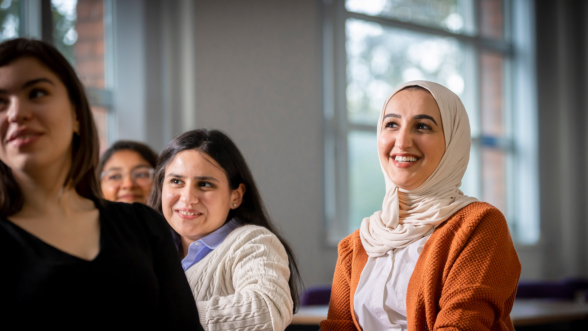 Class full of ladies smiling one of them wearing a white scarf