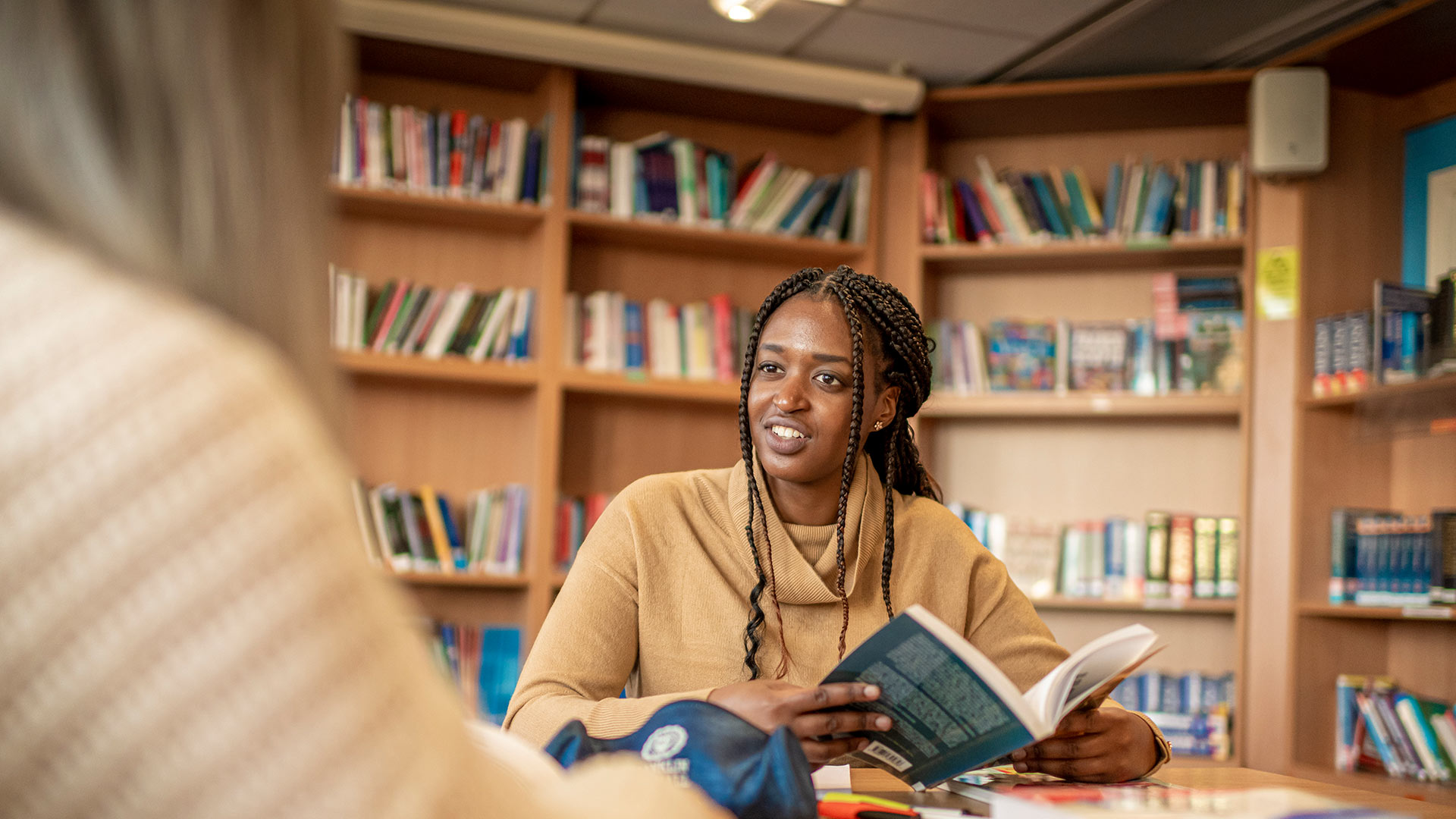 A girl in a library, smiling into the distance whilst holding a book