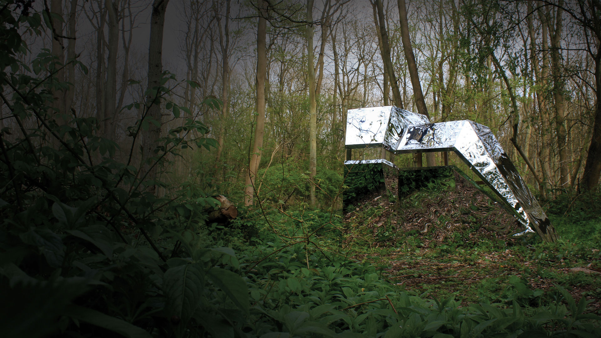 Woods surrounding a mirrored structure art piece, reflecting the ground, sky and trees