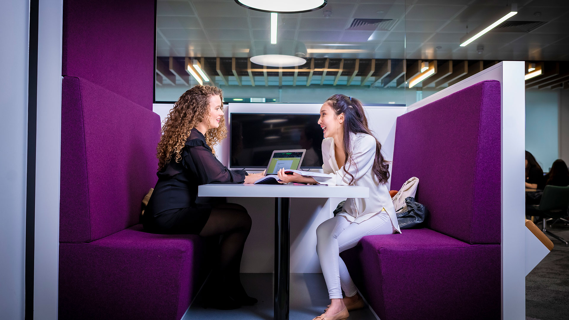 Two students sat round a table in a booth on campus talking to each other