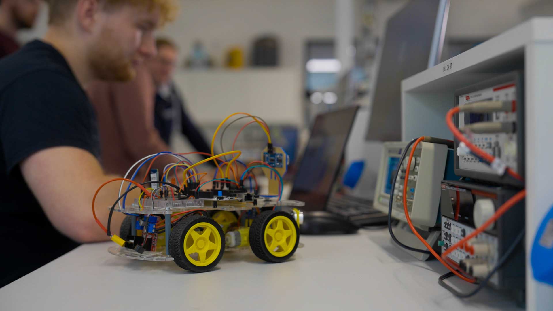 Man working on laptop with model robot car connected next to him