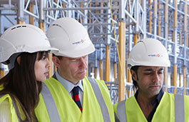 Three people with hardhats and hi-vis vests outside scaffolding