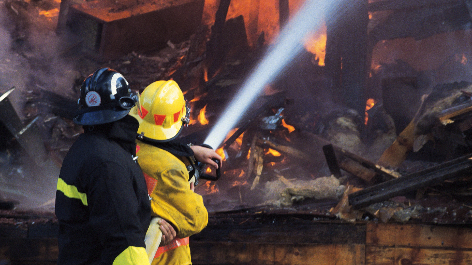 Firefighter with a hose battling a building on fire 