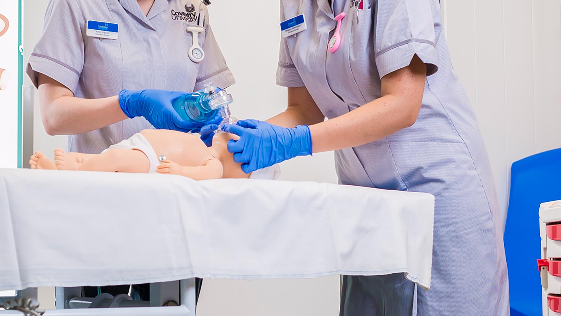 Two nurses putting a breathing mask on a doll lying on a hospital bed 