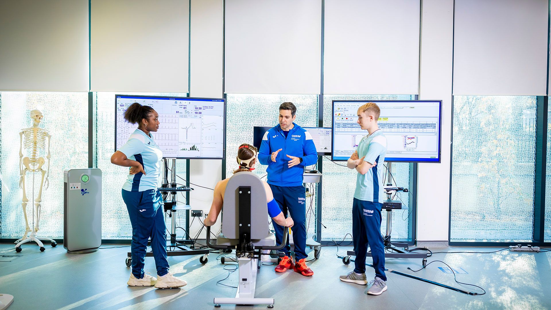 Student on an exercise bike with other students observing and taking notes