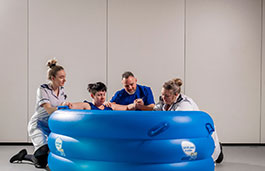 A woman giving birth in a blue water bath with two nurses either side and a visitor behind her for support