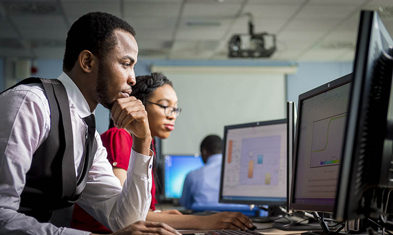 Male and female looking at graphs on two screens