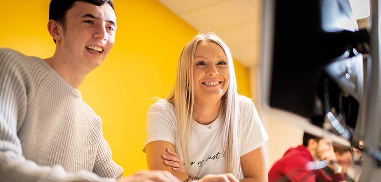 Two smiling students looking at a monitor