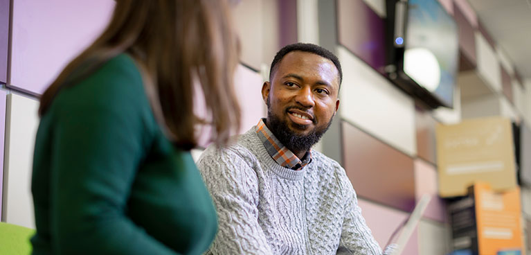 Male student sat inside of a building talking with a female